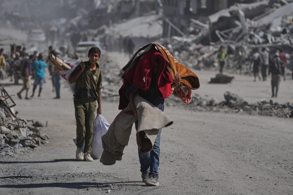 Displaced Palestinians carry their belongings as they walk along the heavily damaged Al-Jalaa Street in Gaza City, Saturday, Oct. 11, 2025, after Israel and Hamas agreed to a pause in their war and the release of the remaining hostages. (AP Photo/Abdel Kareem Hana)