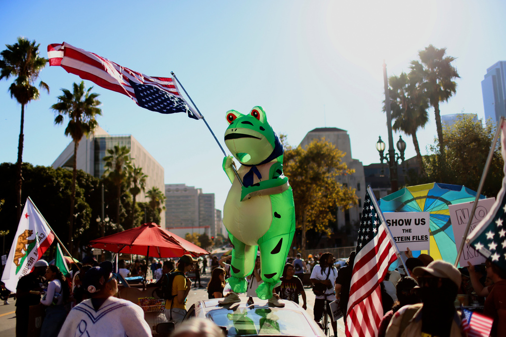 A protester wearing an inflatable frog costume and waving an American flag takes part in a "No Kings" protest Saturday, Oct. 18, 2025, in Los Angeles. (AP Photo/Ethan Swope)