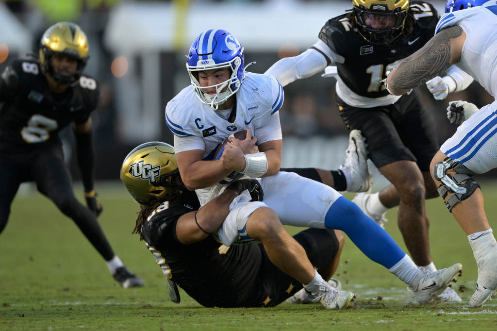 BYU quarterback Bear Bachmeier, center top, is sacked by Central Florida defensive lineman Thomas Collins, center bottom, during the second half of an NCAA college football game, Saturday, Oct. 24, 2026, in Orlando, Fla. (AP Photo/Phelan M. Ebenhack)