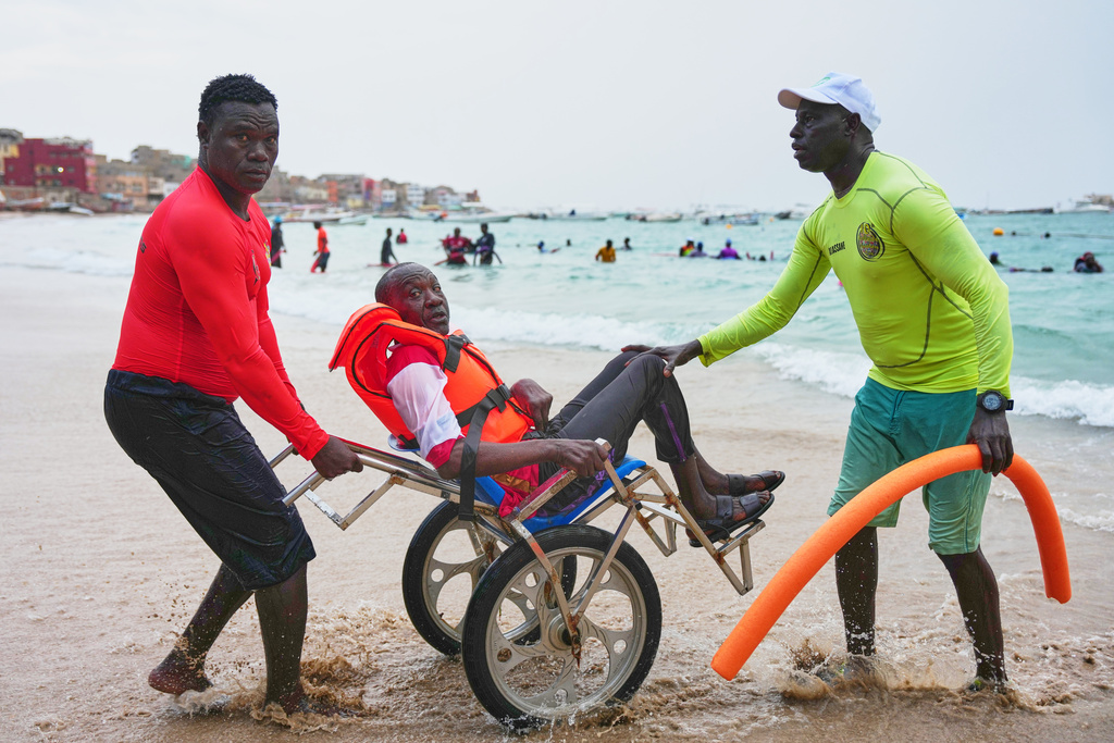 FILE - Instructors assist a participant with limited mobility out of the ocean after an aquatic therapy session in Dakar, Senegal, Saturday, Dec. 6, 2025. (AP Photo/Misper Apawu, File)