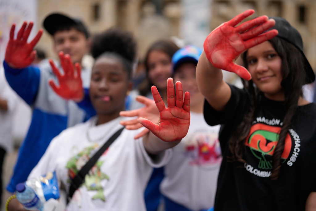 Youths show the paint on their palms after leaving their hand prints on a sheet during an event marking Red Hand Day, also known as the International Day against the Use of Child Soldiers, in Bogota, Colombia, where illegal armed groups recruit children, Thursday, Feb. 12, 2026. (AP Photo/Fernando Vergara)