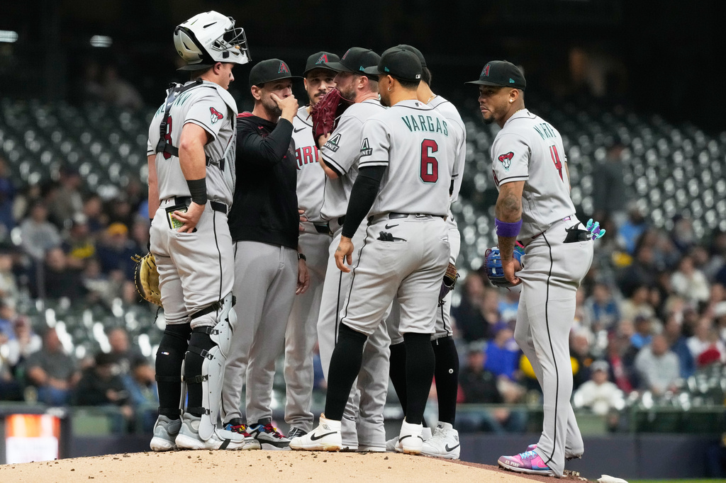 Arizona Diamondbacks pitching coach Brian Kaplan, second from left, talks to starting pitcher Merrill Kelly during the first inning of a baseball game against the Milwaukee Brewers, Tuesday, April 28, 2026, in Milwaukee. (AP Photo/Nam Y. Huh)