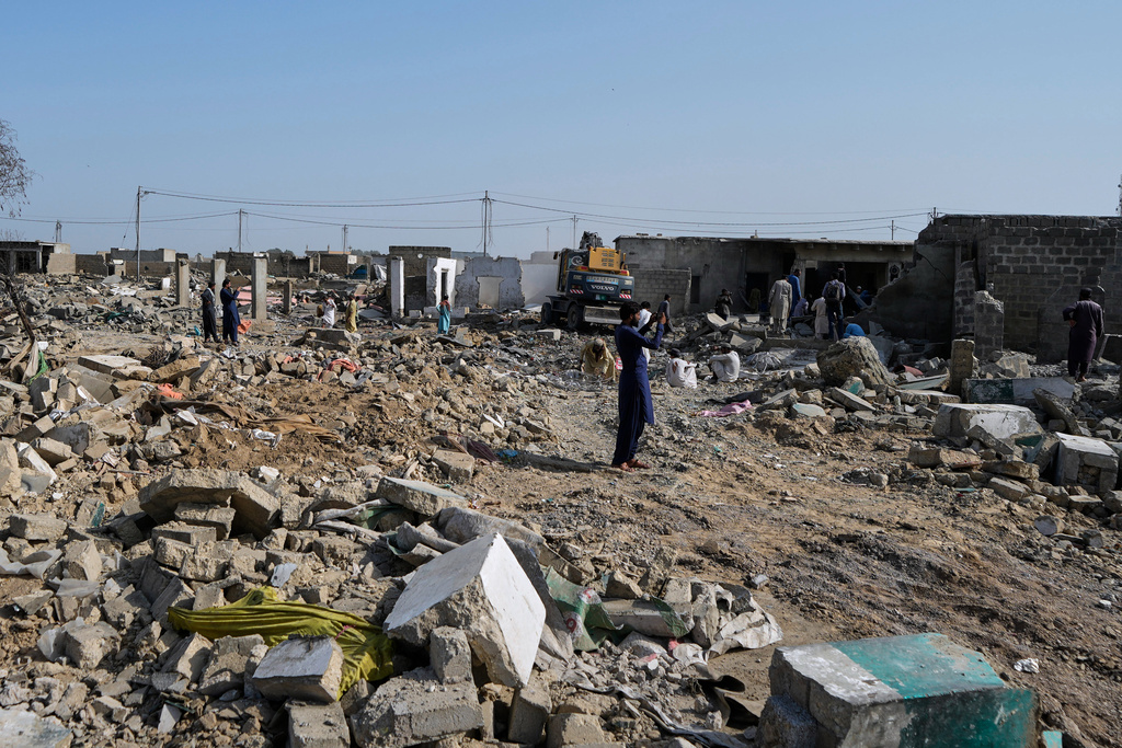 People walk through rubble as a hydraulic shovel demolish a structure during an operation against illegal settlement of Afghan refugees conducted by local government, on the outskirts of Karachi, Pakistan, Wednesday, Oct. 15, 2025. (AP Photo/Fareed Khan)