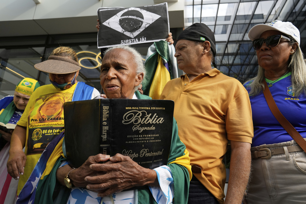 A supporter holding a Bible waits for the arrival of former President Jair Bolsonaro at a hospital, after he was temporarily allowed out of house arrest for medical treatment, in Brasilia, Brazil, Sunday, Sep. 14, 2025. (AP Photo/Eraldo Peres)