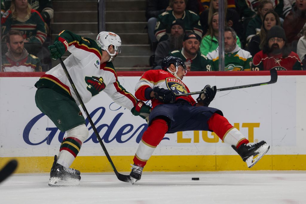 Florida Panthers' Brad Marchand, right, trips while racing Minnesota Wild's Jake Middleton, left, to the puck during the first period of an NHL hockey game, Saturday, Jan. 24, 2026, in St. Paul, Minn. (AP Photo/Lily Dozier)
