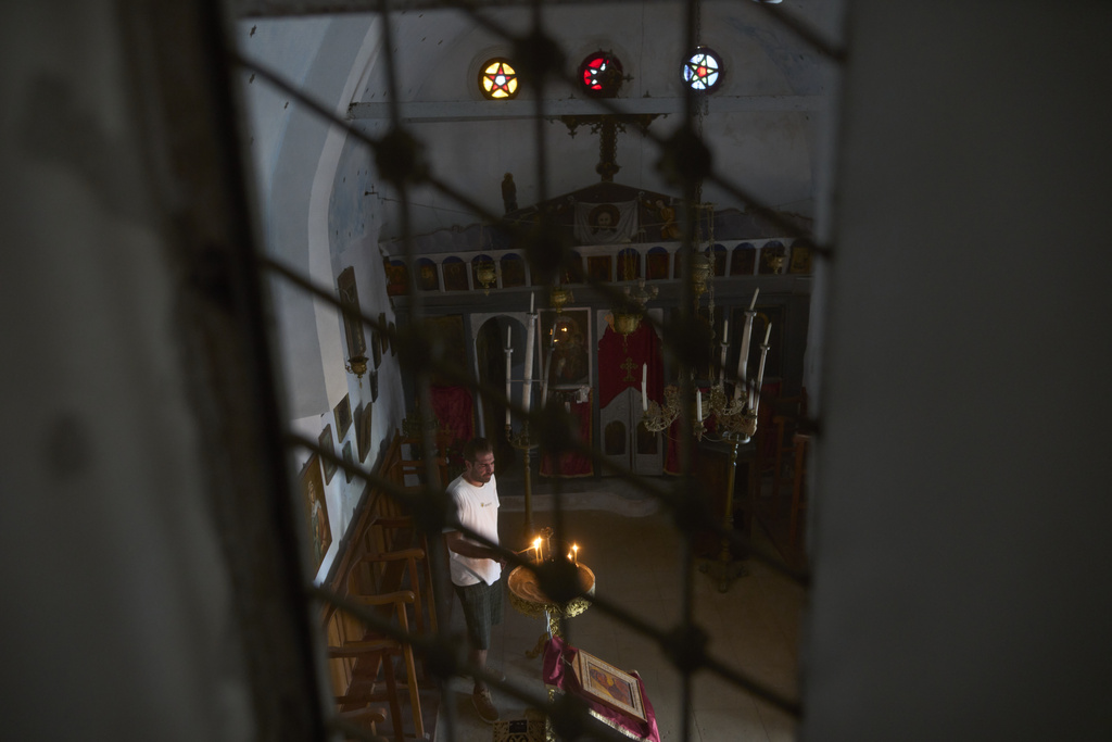 Konstantinos Vasilopoulos lights a candle at the Panagia Faneromeni family-owned chapel near the village of Triantaros, on the island of Tinos, Greece, Saturday, Sept. 6, 2025. (AP Photo/Petros Giannakouris)