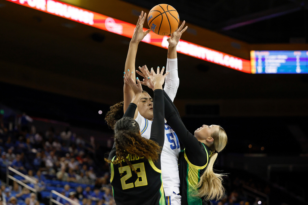 UCLA center Lauren Betts (51) looks to pass the ball while guarded by Oregon forward Sarah Rambus (23) and guard Sammie Wagner, right, during the first half of an NCAA college basketball game Sunday, Dec. 7, 2025, in Los Angeles. (AP Photo/Caroline Brehman)