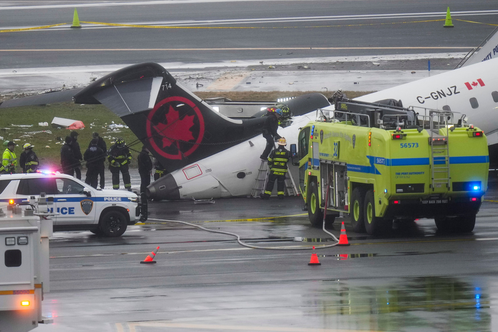 Firefighters and investigators examine the site, Monday, March 23, 2026, where an Air Canada jet came to rest after colliding with a Port Authority firetruck at LaGuardia Airport, after landing Sunday night in New York. (AP Photo/Seth Wenig)