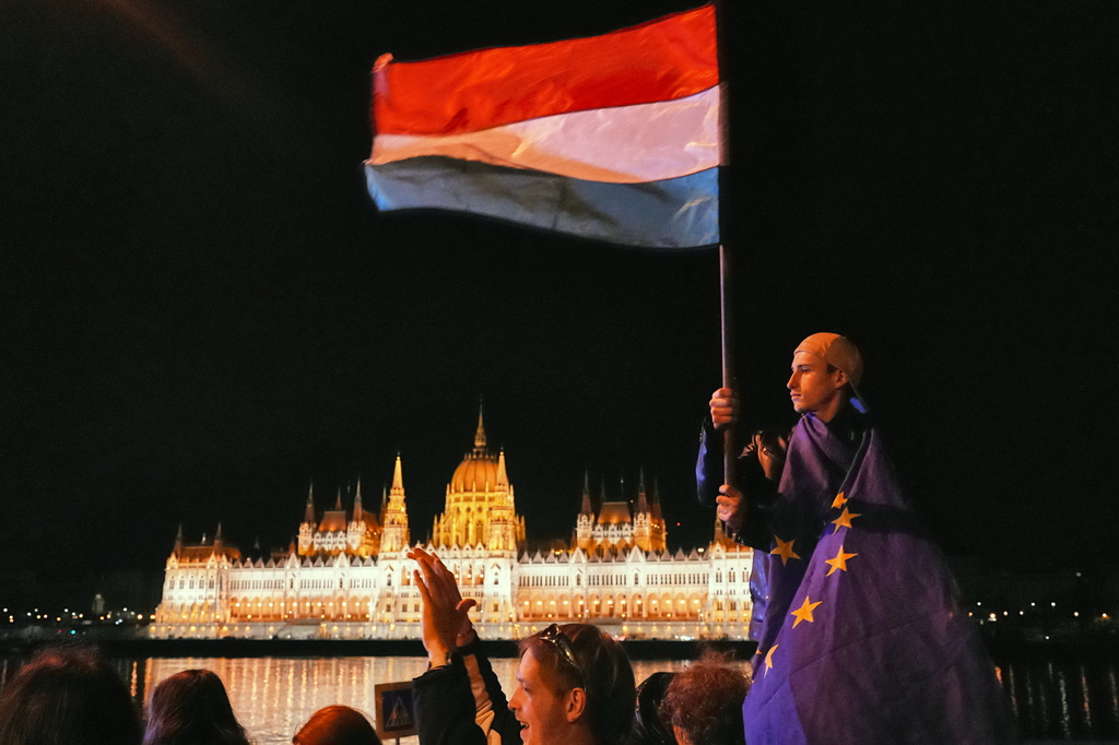 A man wrapped in the European Union flag waves a Hungarian flag, backdropped by the parliament building, early Monday April 13, 2026 as people celebrate Peter Magyar ousting Prime Minister Viktor Orban after 16 years in power. (AP Photo/Sam McNeil)