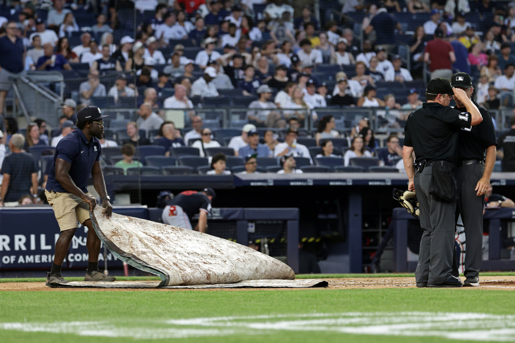 A member of the grounds crew, left, covers the field behind the umpires, right, as the Minnesota Twins and the New York Yankees enter a rain delay during the third inning of a baseball game Friday, July 3, 2026, in New York. (AP Photo/Adam Hunger)