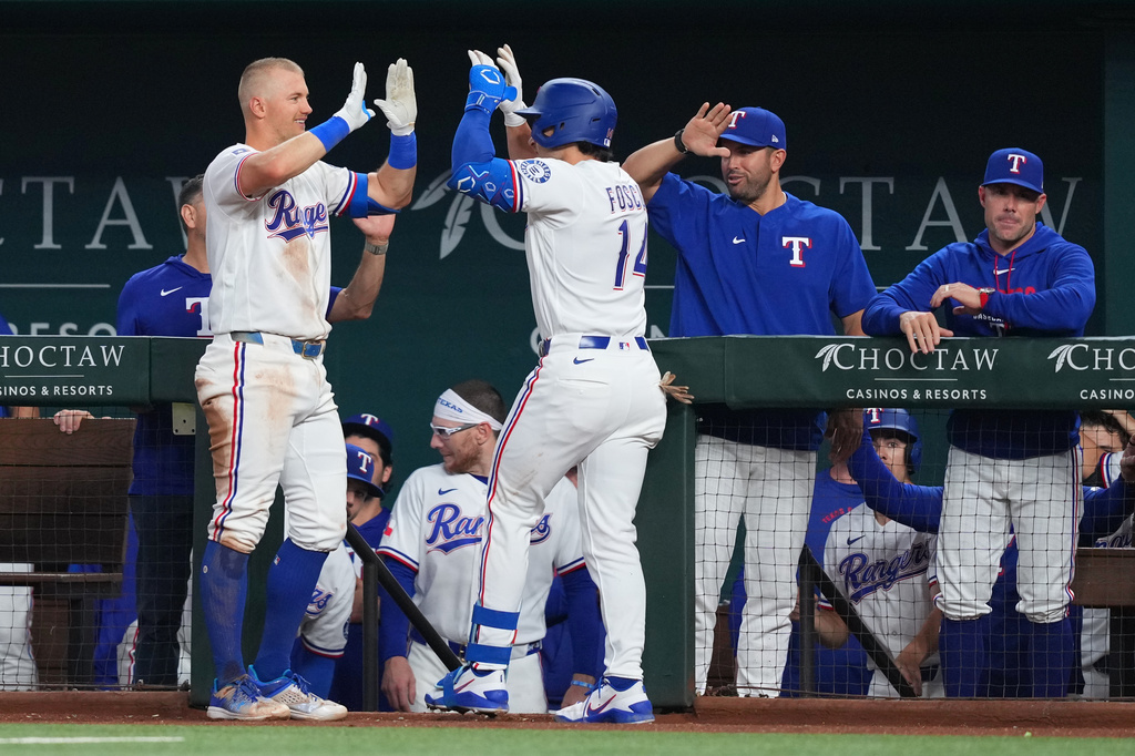 Texas Rangers' Justin Foscue, center right, is greeted by Josh Jung near the dugout after hitting his first career home run during the third inning of a baseball game against the Chicago Cubs, Saturday, May 9, 2026, in Arlington, Texas. (AP Photo/Julio Cortez)