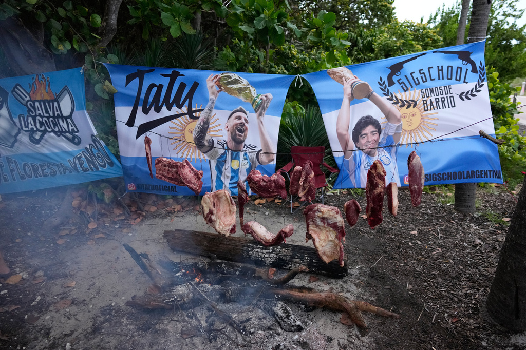 Argentine Angus beef hangs suspended over an outdoor fire as Argentina fans gather to celebrate and cheer on their team at a beachfront park in Miami Beach, Fla., Thursday, July 2, 2026, one day ahead of their World Cup round of 32 soccer match against Cape Verde. (AP Photo/Rebecca Blackwell)