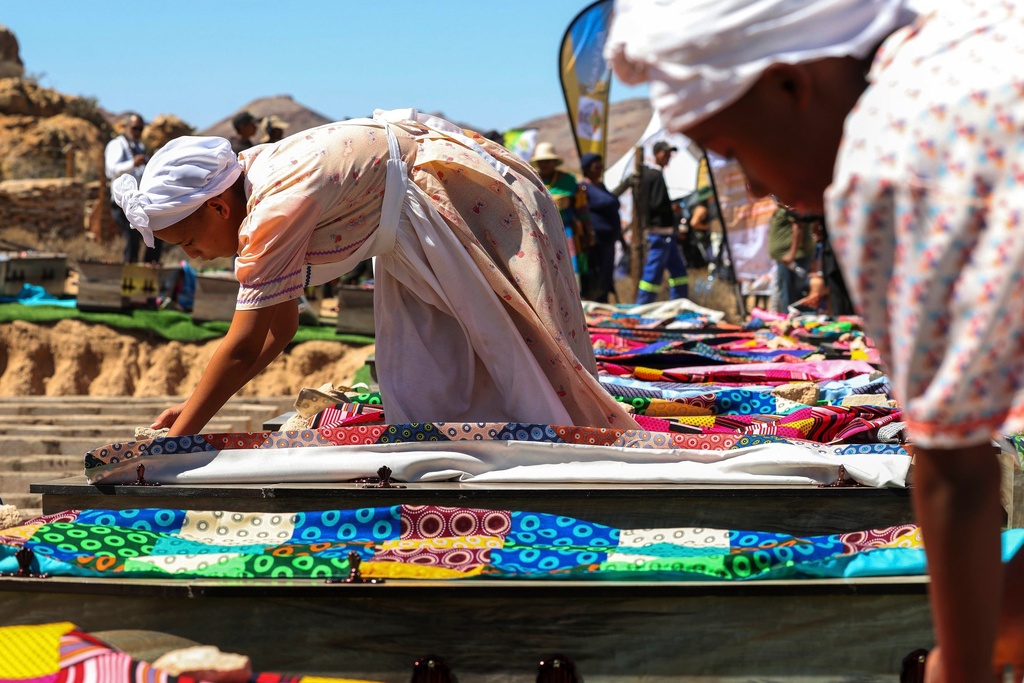 In this photo provided by the South African Government Communications and Information Services, women draping coffins with traditional cloth during a reburial of remains of dozens of Africans whose bodies were dug up and sent to Europe for scientific research long ago, in Steinkopf, South Africa, Monday, March 23, 2026. (Jairus Mmutle/GCIS via AP)