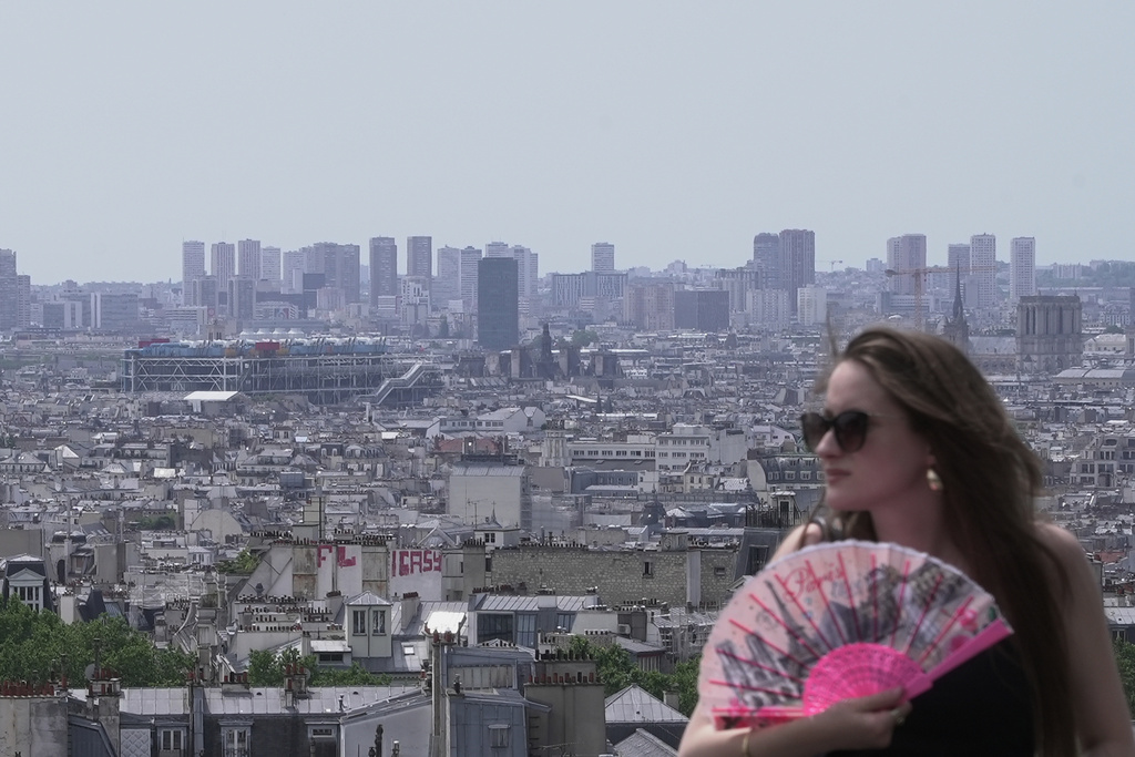 A woman holds a fan as the roofs of Paris are seen background, Tuesday, June 23, 2026. (AP Photo/John Leicester)
