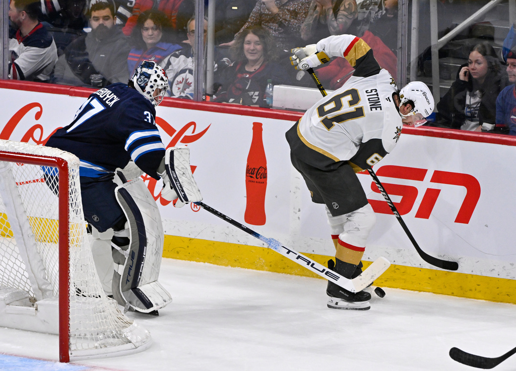 Vegas Golden Knights' Mark Stone (61) and Winnipeg Jets goaltender Connor Hellebuyck (37) attempt to control a loose puck behind the net during the third period of their NHL hockey game in Winnipeg, Tuesday Jan. 6, 2026. (Fred Greenslade/The Canadian Press via AP)