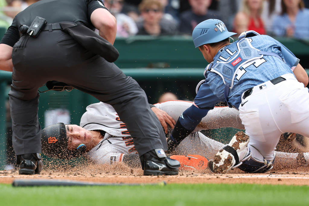 San Francisco Giants' Jung Hoo Lee is tagged out at home plate by Washington Nationals catcher Drew Millas while attempting to score on double hit by San Francisco Giants' Heliot Ramos against pitcher Cade Cavalli during the second inning of a baseball game, Saturday, April 18, 2026, in Washington. (AP Photo/Terrance Williams)
