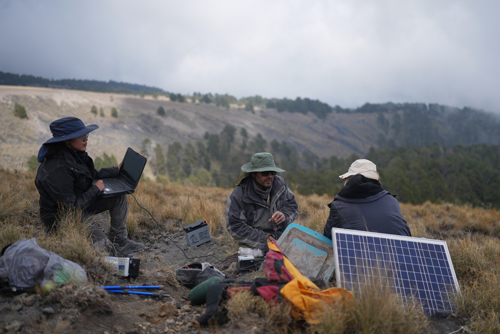 Karina Rodriguez, left, a master's student, and Marco Calo, center, a geophysicist at the National Autonomous University of Mexico (UNAM), collect information from a monitoring station on the slopes of the Popocatepetl volcano in Mexico, Friday, Dec. 5, 2025. (AP Photo/Eduardo Verdugo)