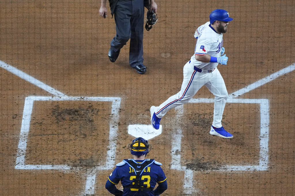 Texas Rangers' Jake Burger, right, crosses home plate in front of Milwaukee Brewers catcher Danny Jansen after hitting a solo home run off starting pitcher Freddy Peralta during the second inning of a baseball game Wednesday, Sept. 10, 2025, in Arlington, Texas. (AP Photo/Julio Cortez)
