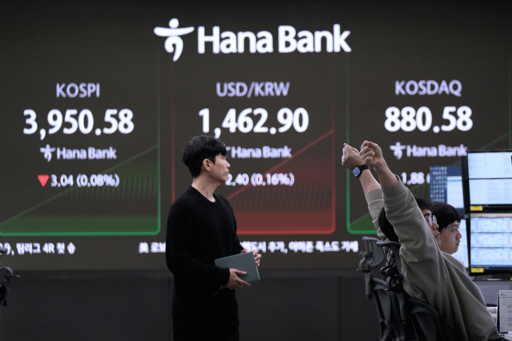 A currency trader stretches near a screen showing the Korea Composite Stock Price Index (KOSPI), left, and the foreign exchange rate between U.S. dollar and South Korean won, center, at the foreign exchange dealing room of the Hana Bank headquarters in Seoul, South Korea, Wednesday, Nov. 19, 2025. (AP Photo/Ahn Young-joon)