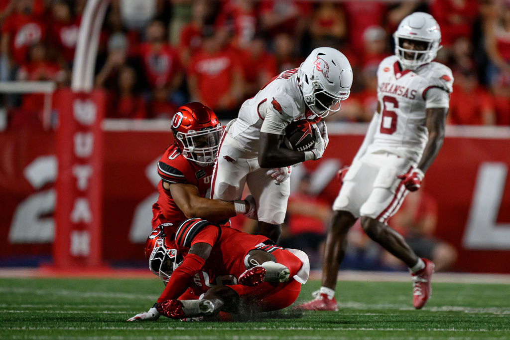 Arkansas wide receiver Jamari Hawkins, center, runs the ball after a catch tackled by Utah linebacker Cyrus Polu, center left, and cornerback James Chenault Jr., bottom, during the first half of an NCAA college football game Saturday, Sept. 12, 2026, in Salt Lake City. (AP Photo/Tyler Tate)