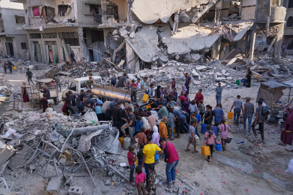 Palestinians collect water from a truck amid the destruction caused by the Israeli air and ground offensive in Gaza City, Thursday, Oct. 16, 2025. (AP Photo/Jehad Alshrafi)