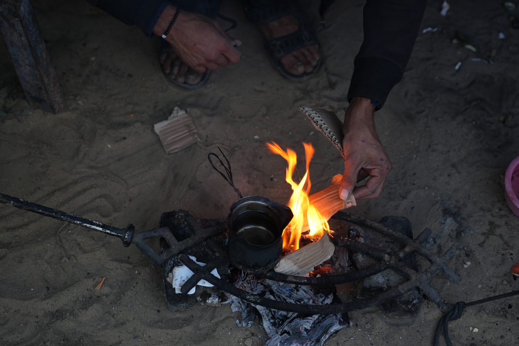 Displaced Palestinian Amr Al-Manaya, 35, sits by the fire with his children, next to their tent in Deir al-Balah, Gaza Strip, Saturday, Jan. 17, 2026. (AP Photo/Abdel Kareem Hana)