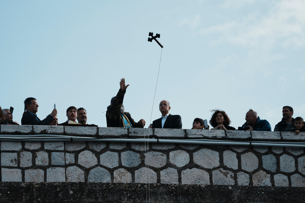 People attend the Epiphany ceremony as a Greek Orthodox priest, center, throws a cross blessing the waters at Lake Marathon, near Athens, on Tuesday, Jan. 6, 2026, where receding water levels reflect successive years of low rainfall across Greece. (AP Photo/Thanassis Stavrakis)
