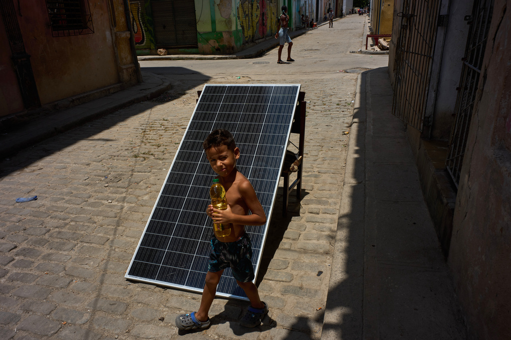 A child walks with a bottle of oil past a solar panel set up on the street to charge batteries during a blackout in Havana, Cuba, Monday, July 6, 2026. (AP Photo/Ramon Espinosa)