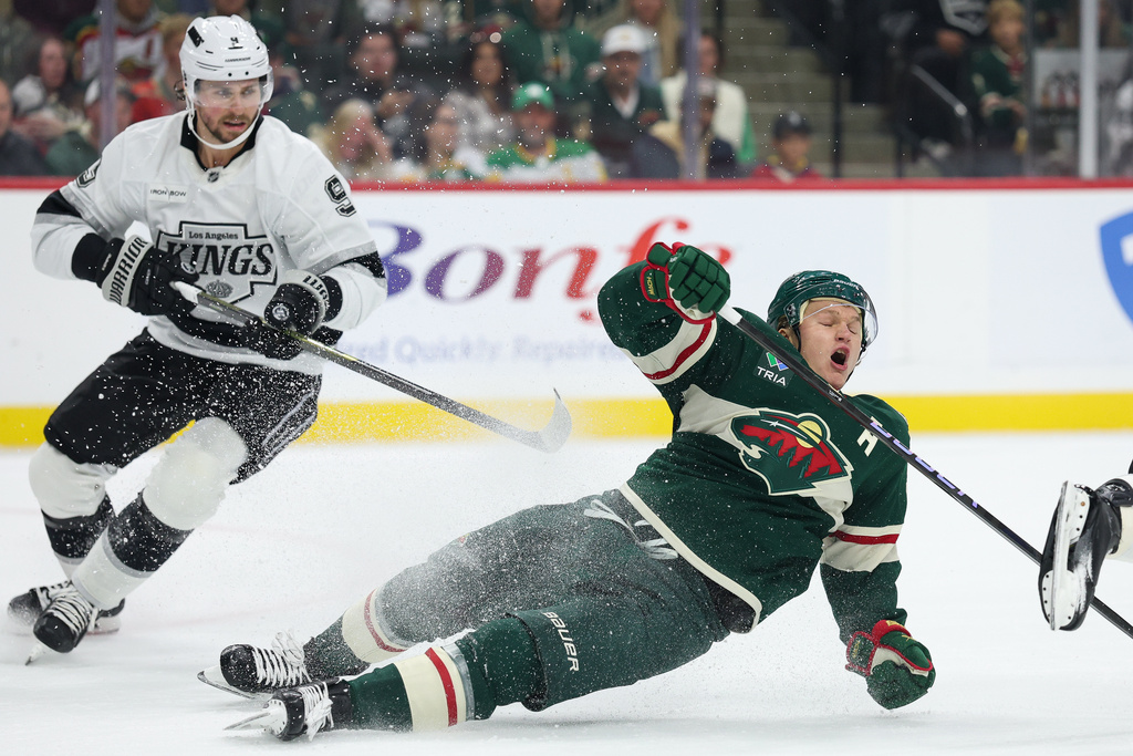 Los Angeles Kings right wing Adrian Kempe, left, commits a hooking penalty against Minnesota Wild left wing Kirill Kaprizov, right, during the first period of an NHL hockey game Monday, Oct. 13, 2025, in St. Paul, Minn. (AP Photo/Matt Krohn)