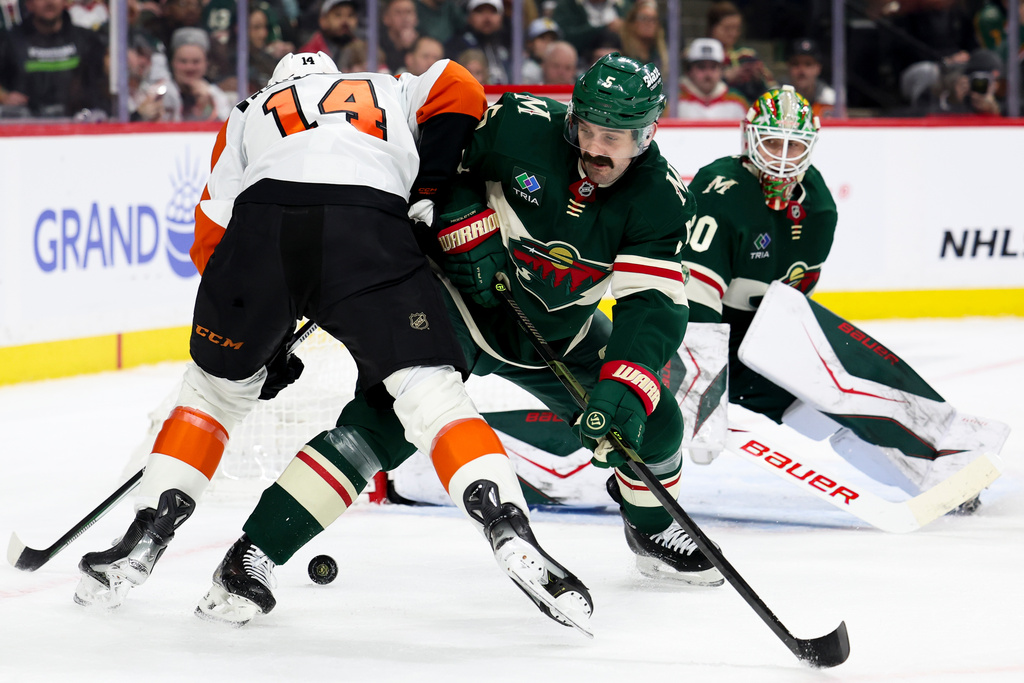 Minnesota Wild defenseman Jake Middleton (5) knocks the puck away from Philadelphia Flyers center Sean Couturier (14) during the second period of an NHL hockey game Thursday, March 12, 2026, in St. Paul, Minn. (AP Photo/Ellen Schmidt)