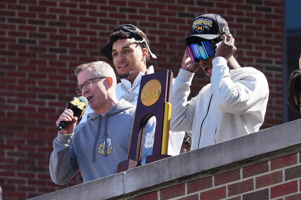 Michigan head coach Dusty May, left, talks to fans as Yaxel Lendeborg, center, and L.J. Cason, right, listen as the team returns to campus Tuesday, April 7, 2026, in Ann Arbor, Mich., the day after defeating UConn at the Final Four of the NCAA college basketball tournament. (AP Photo/Paul Sancya)