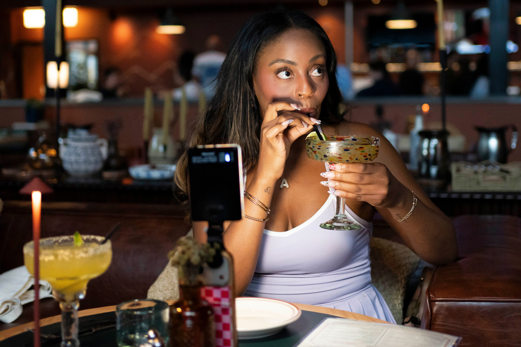 Phoenix-based content creator Aiesha Beasley films herself as she samples a margarita during the grand opening of Padeland, a venue for the racket sport padel in Chandler, Ariz., Thursday, Aug. 13, 2026. (AP Photo/Rebecca Noble)