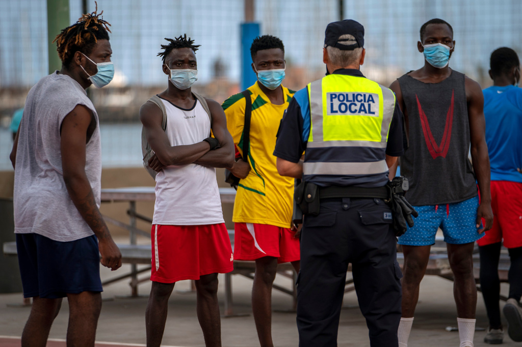 FILE - A police officer speaks with migrants and asylum-seekers in Gran Canaria island, Spain, Tuesday, Aug. 18, 2020. (AP Photo/Emilio Morenatti, File)