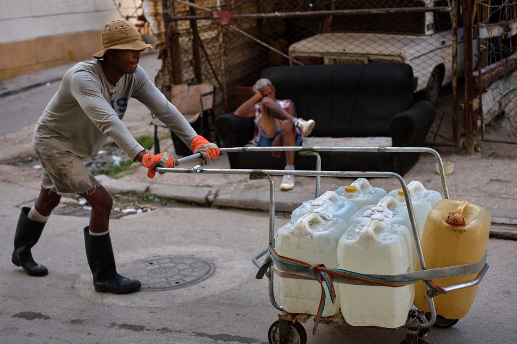 A man pushes a cart filled with water containers while another man rests on a sofa on a street in Havana, Cuba, Thursday, Aug. 27, 2026. (AP Photo/Ramon Espinosa)