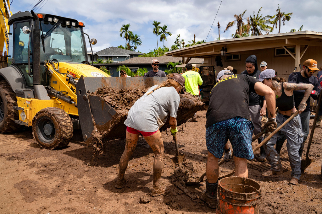 Volunteers shovel mud and debris from a flooded residential neighborhood, Tuesday, March 24, 2026, in Waialua, Hawaii. (AP Photo/Mengshin Lin)