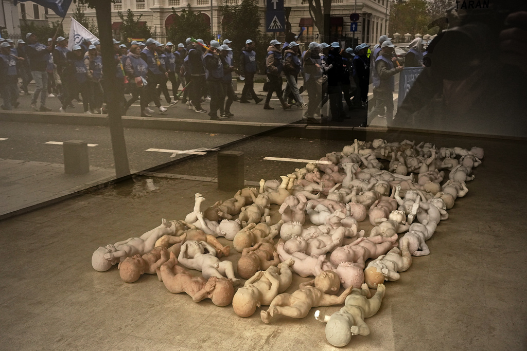 Marching trade union members are reflected in an art galley window, displaying an installation on human condition by sculptor Lucian Taran, as they protest against the government's austerity measures in Bucharest, Romania, Wednesday, Nov. 12, 2025. (AP Photo/Andreea Alexandru)