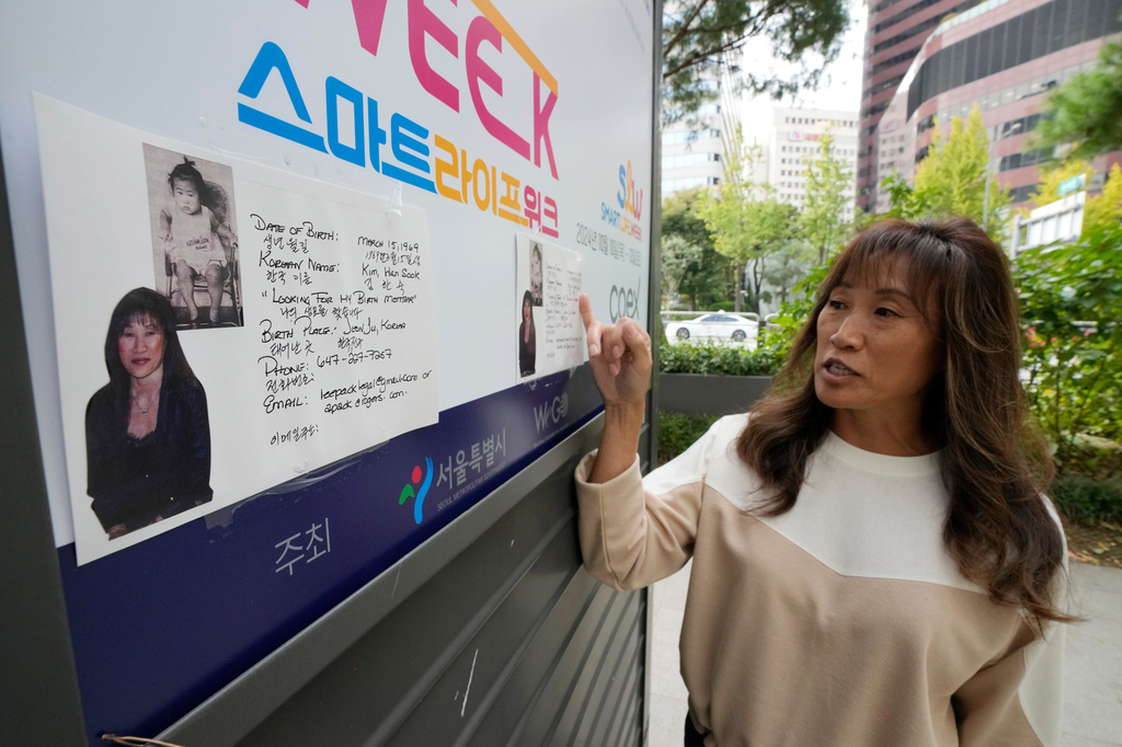 Angela Lee-Pack, a Korean adoptee from Canada, explains flyers with her photos attached to a newspaper stand during an interview with The Associated Press on a street in Seoul, South Korea, on Oct. 21, 2024. (AP Photo/Ahn Young-joon)