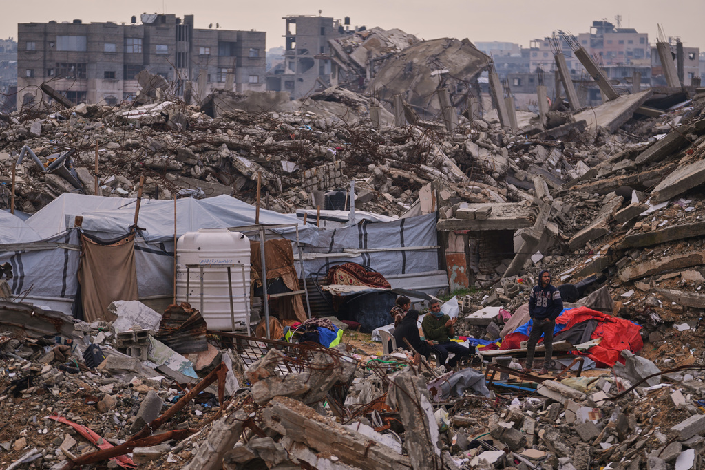 Palestinians stand next to a tent set up on the rubble of buildings destroyed during Israeli air and ground operations in the Sheikh Radwan neighborhood, in Gaza City, Tuesday, Dec. 30, 2025. (AP Photo/Abdel Kareem Hana)