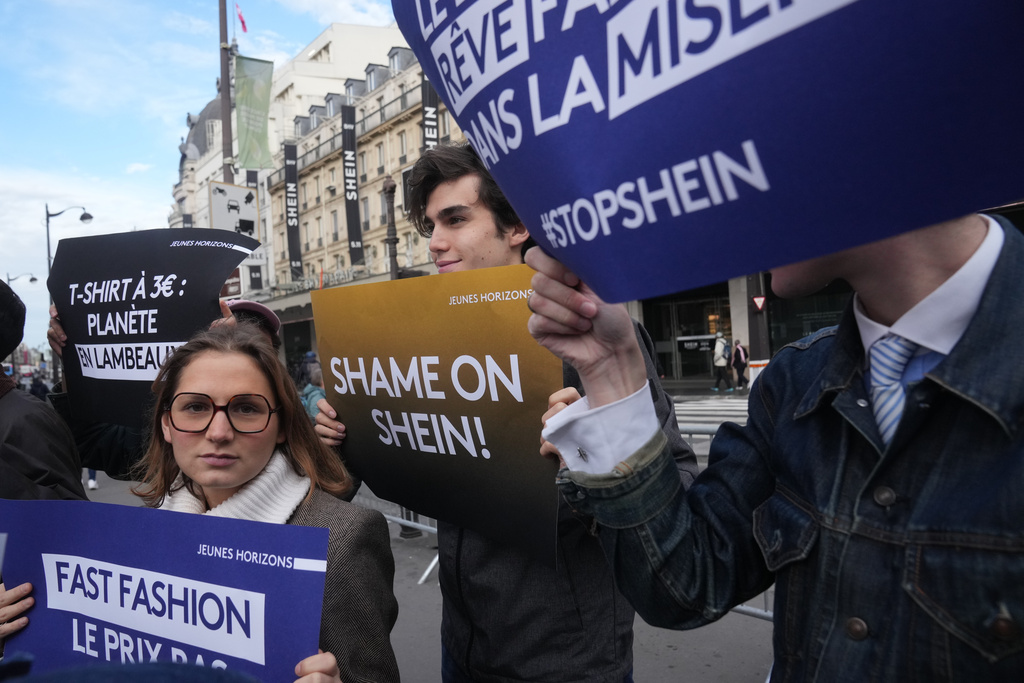 Demonstrators holds posters outside the BHV department store where fast fashion powerhouse Shein's first permanent store is set to open, Wednesday, Nov. 5, 2025 in Paris. (AP Photo/Thibault Camus)