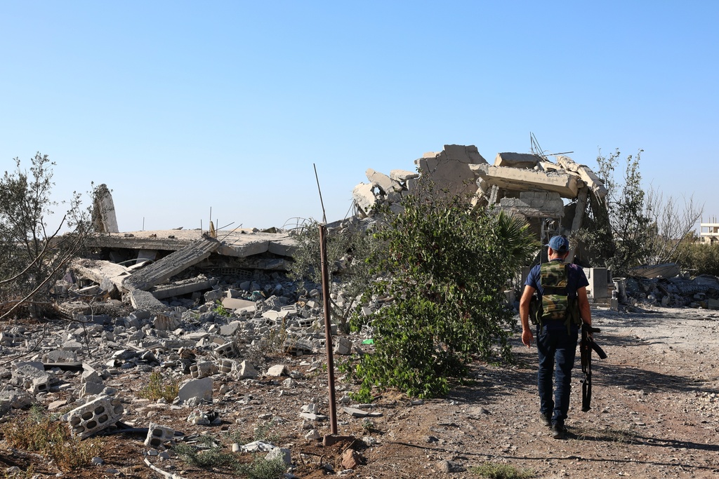 A gunman walks by the remains of a house destroyed during the recent sectarian clashes in the Druze-majority town of Sweida, southern Syria, on Sept. 19, 2025. (AP Photo/Fahd Kiwan)