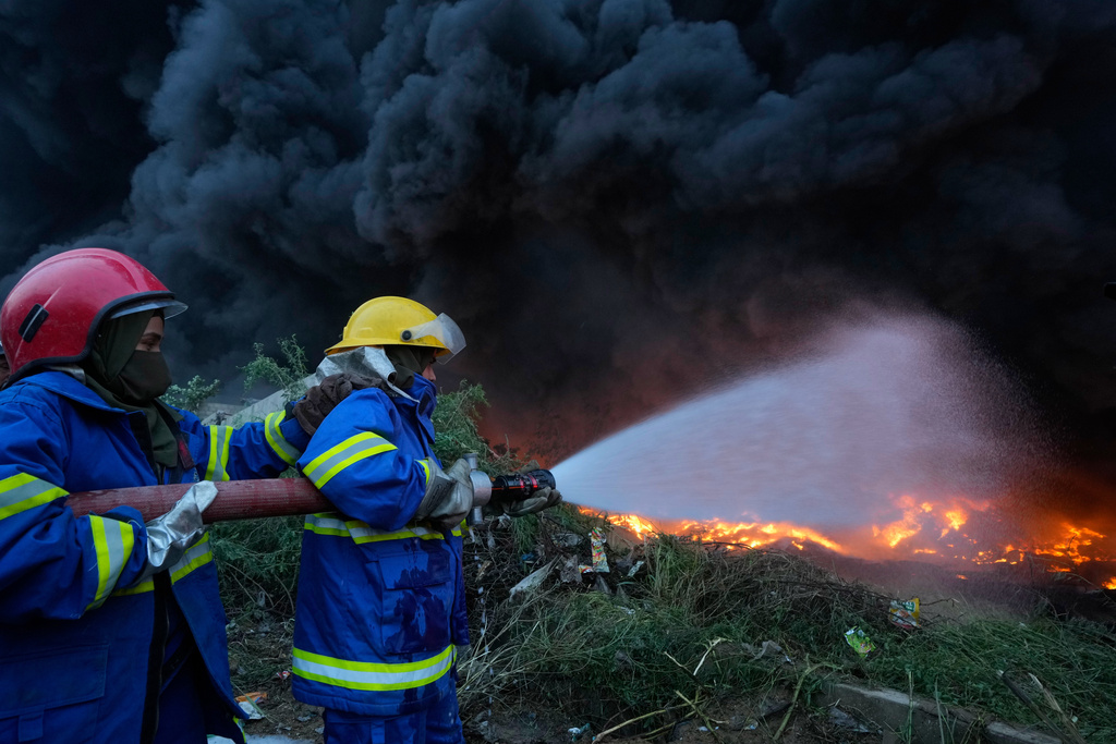 Female firefighter Syeda Masooma Zaidi, right, with her team member spray water to extinguish on a fire broke out in a storage facility packed vehicles tires, outskirts of Karachi, Pakistan, Thursday, Oct. 30, 2025. (AP Photo/Fareed Khan)