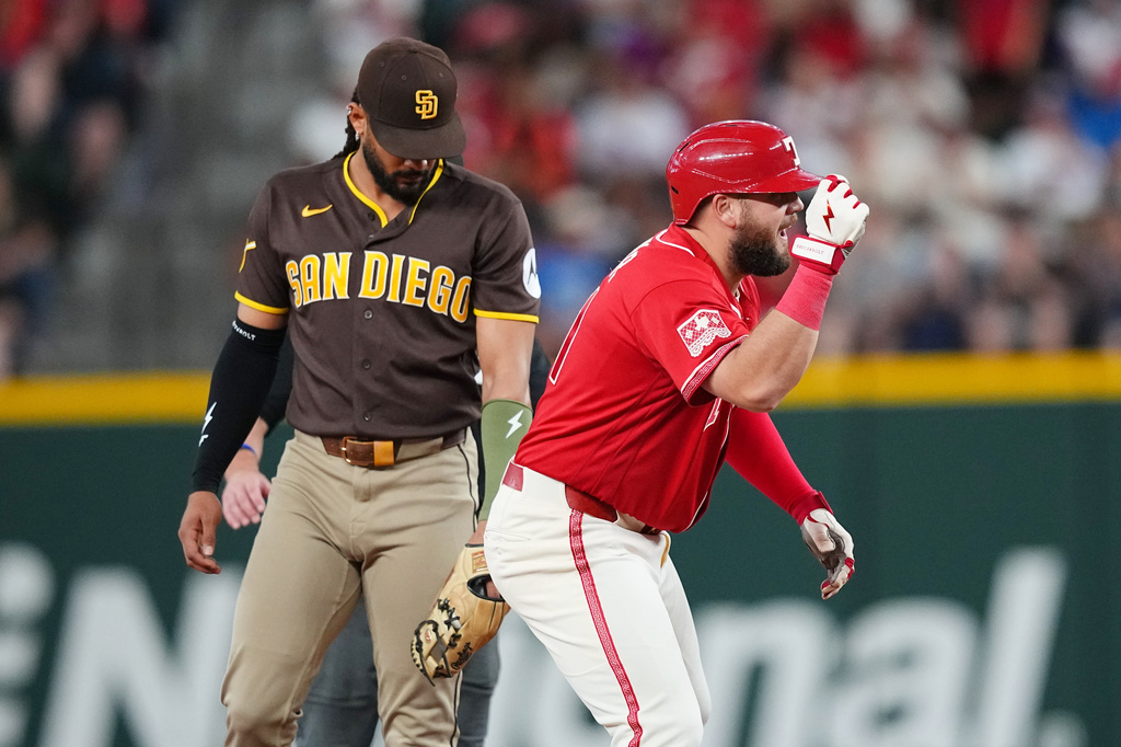 Texas Rangers' Jake Burger, right, reacts in front of San Diego Padres second baseman Fernando Tatis Jr. after hitting an RBI double to score Alejandro Osuna and Ezequiel Duran during the first inning of a baseball game, Friday, June 19, 2026 in Arlington, Texas. (AP Photo/Julio Cortez)