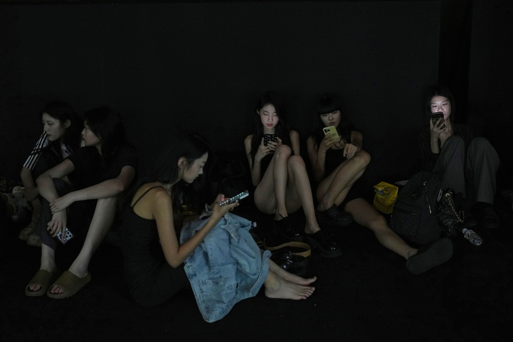 Models browse their smartphones as they rest in the backstage during the SS2026 China Fashion Week in Beijing, Sunday, Sept. 7, 2025. (AP Photo/Andy Wong)