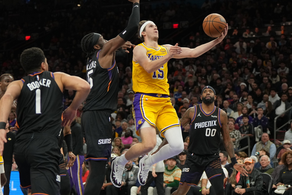 Los Angeles Lakers guard Austin Reaves drives between Phoenix Suns guard Devin Booker, center Mark Williams (15), and forward Royce O'Neale (00) during the first half of an NBA basketball game, Tuesday, Dec. 23, 2025, in Phoenix. (AP Photo/Rick Scuteri)