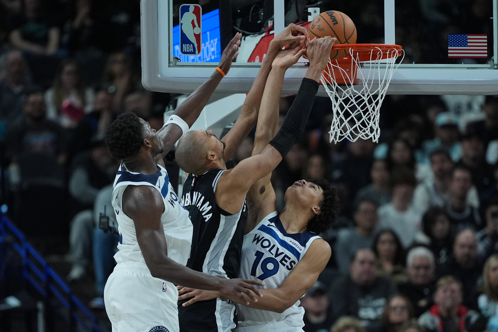 San Antonio Spurs forward Victor Wembanyama, center, scores against Minnesota Timberwolves guard Anthony Edwards, left, and forward Joan Beringer (19) during the second half of an NBA basketball game in San Antonio, Saturday, Jan. 17, 2026. (AP Photo/Eric Gay)
