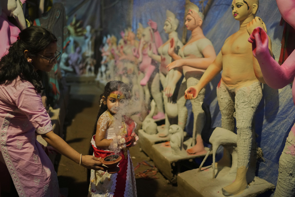 A woman uses smoke as a prop to photograph her child, who is dressed as the Hindu goddess Durga, at a temporary shelter where idols of Hindu gods and goddesses are being made ahead of the Durga Puja festival, in New Delhi, India, Friday, Sept. 19, 2025. (AP Photo/Manish Swarup)