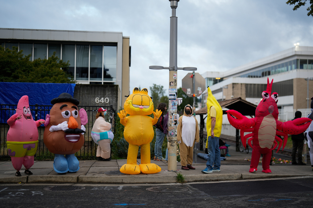 People wearing costumes protest outside a U.S. Immigration and Customs Enforcement facility, at right, on Saturday, Oct. 11, 2025, in Portland, Ore. (AP Photo/Jenny Kane)