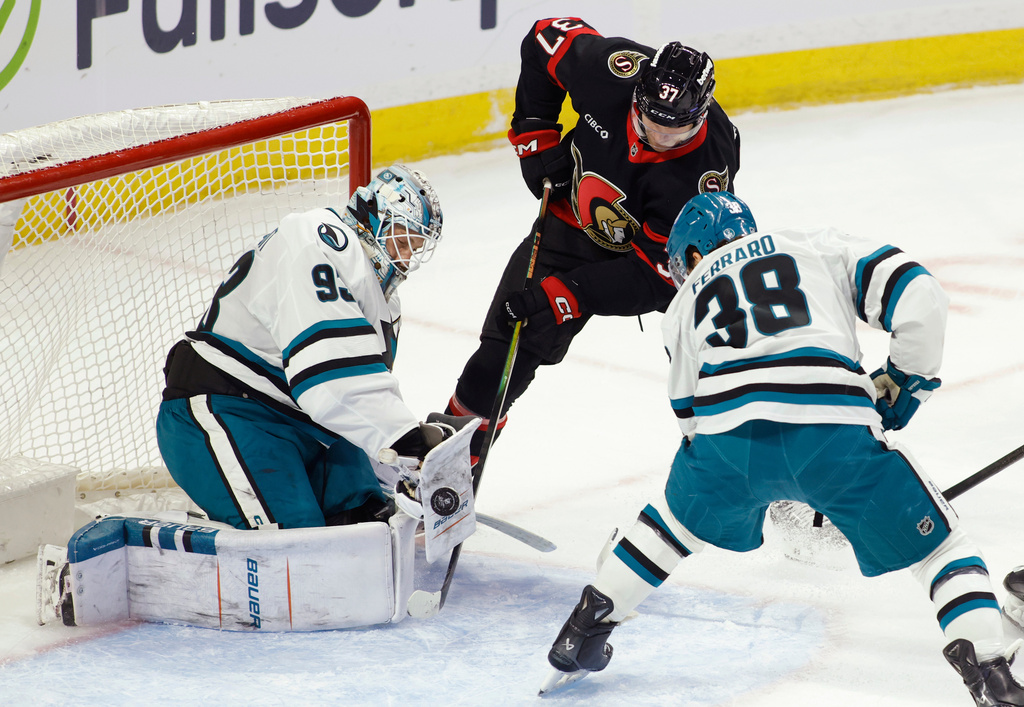 San Jose Sharks' goaltender Laurent Brossoit (93) makes a save on Ottawa Senators' Warren Foegele (37) as San Jose Sharks' Mario Ferraro (38) looks on during first period NHL hockey action in Ottawa on Sunday, March 15, 2026. (Patrick Doyle/The Canadian Press via AP)