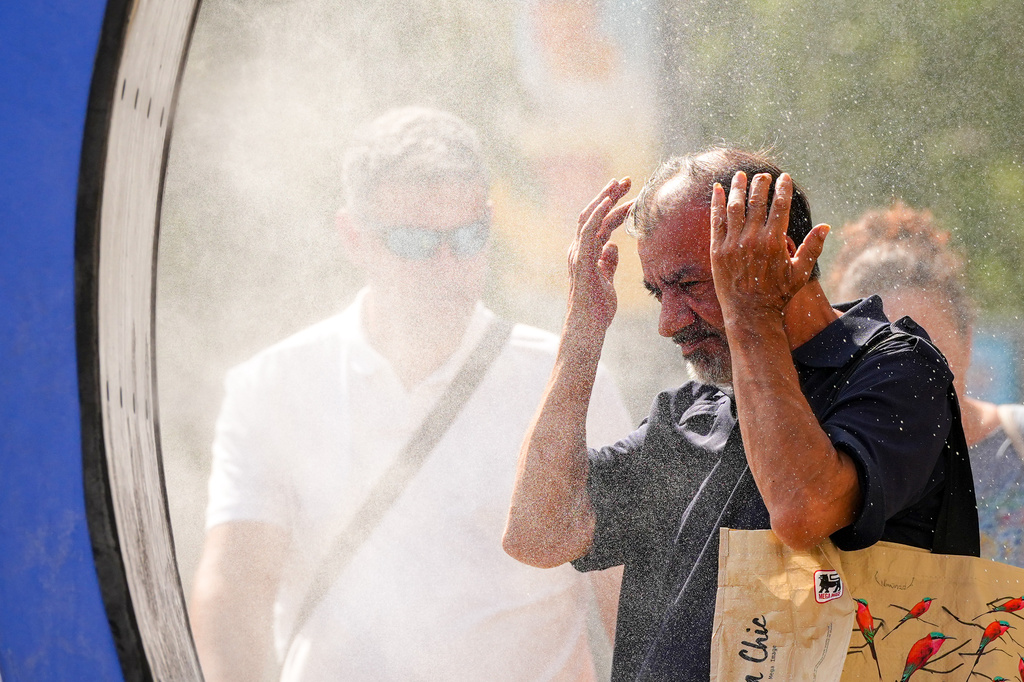 A man splashes water on his face as he walks through a water mist machine installed by city administration to assist people in coping with the heat, as the National Weather forecaster issued an extreme heat code red warning for most parts of the country, in Bucharest, Romania, Thursday, Aug. 6, 2026. (AP Photo/Vadim Ghirda)