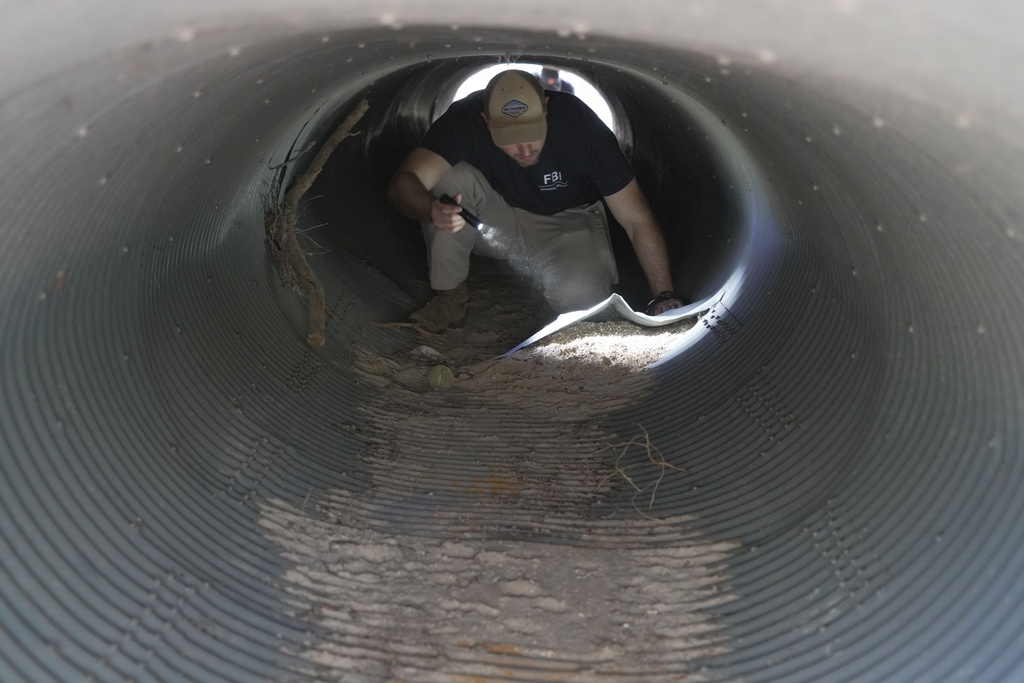 An investigator looks inside a culvert in the neighborhood where Annie Guthrie, whose mother Nancy Guthrie has been missing for more than a week, lives just outside Tucson, Ariz., on Tuesday, Feb. 10, 2026. (AP Photo/Ty ONeil)